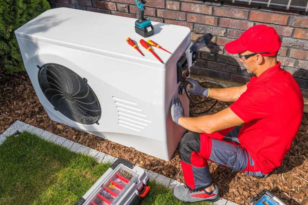 HVAC technician in red and gray uniform installing a residential heat pump unit outdoors