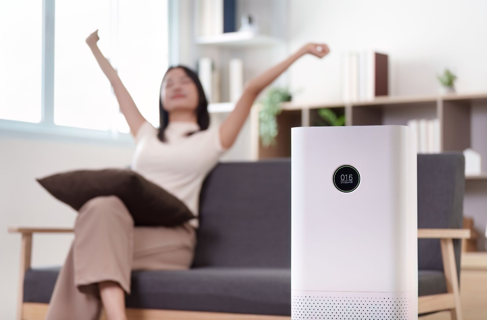 Woman stretches her arms while sitting on a couch in a modern living room with an air purifier