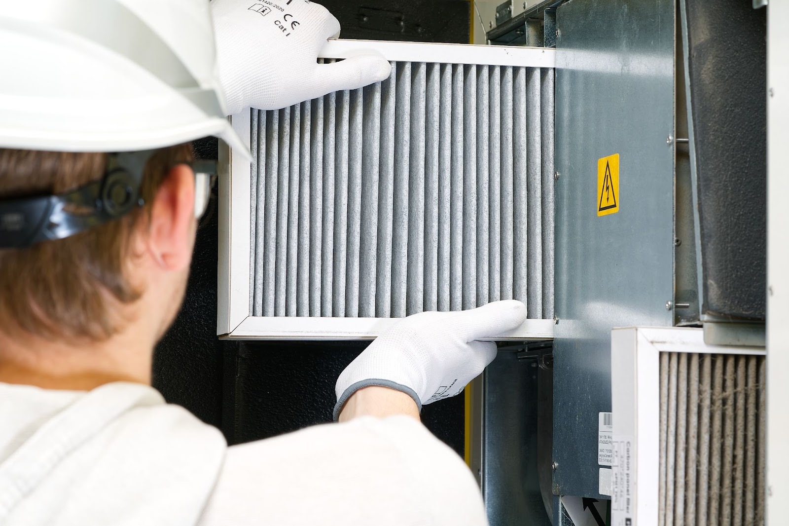 Rear view of an HVAC technician replacing a dirty air filter in a residential central air conditioning system