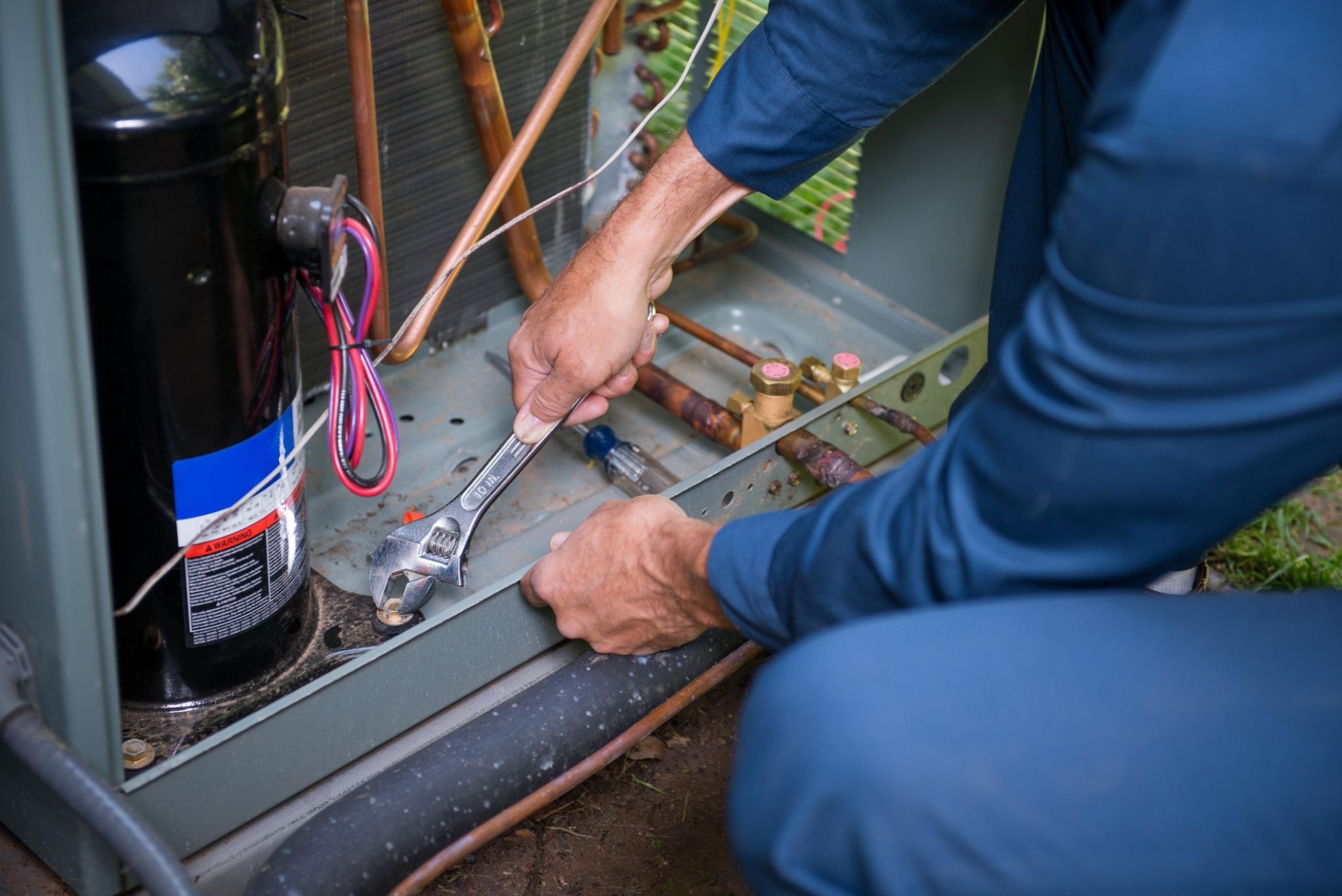 Detailed view of an HVAC technician fixing an outdoor air conditioning unit with an adjustable wrench